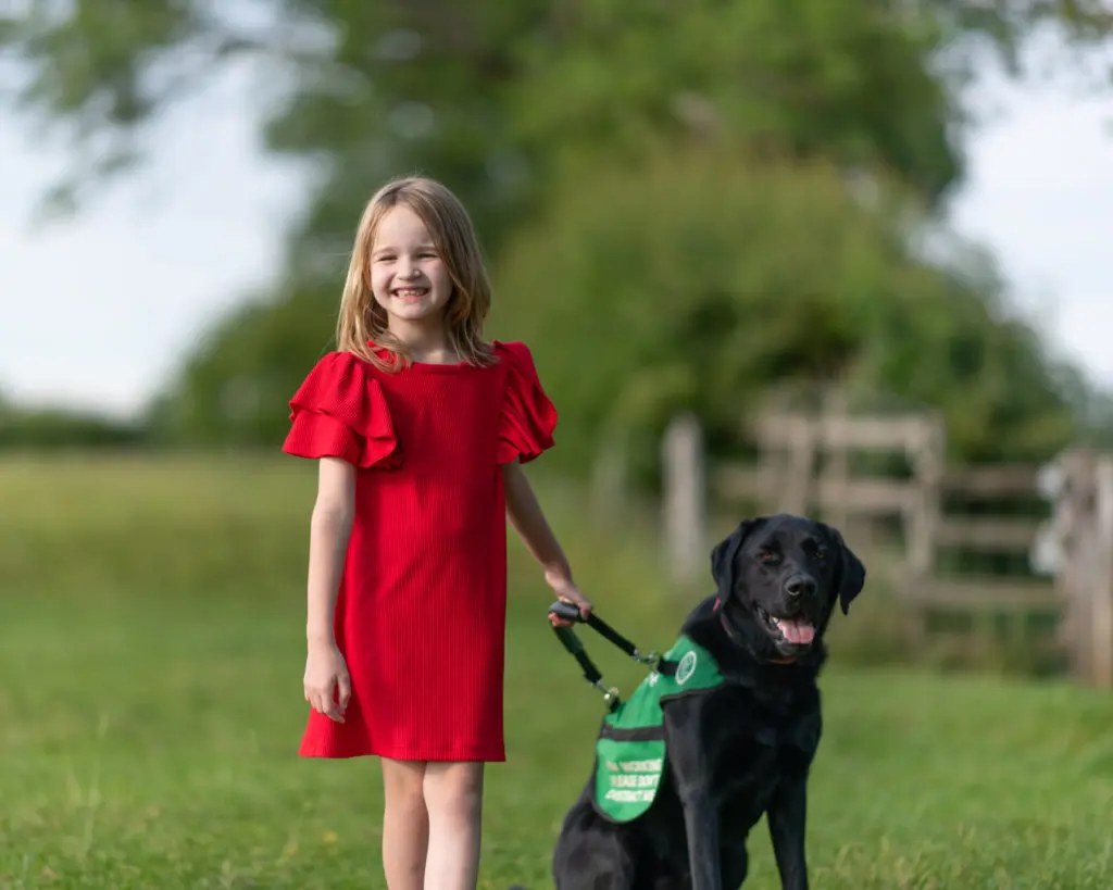 Emily is wearing a red dress and standing next to her autism assistance dog Oslo holding his harness