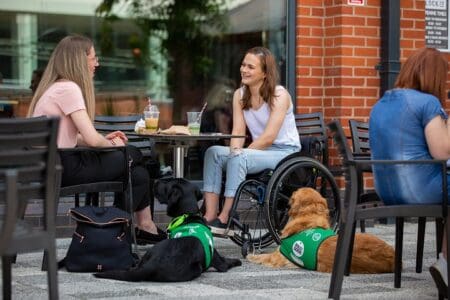 Two women enjoying a coffee with their assistance dogs lying next to them