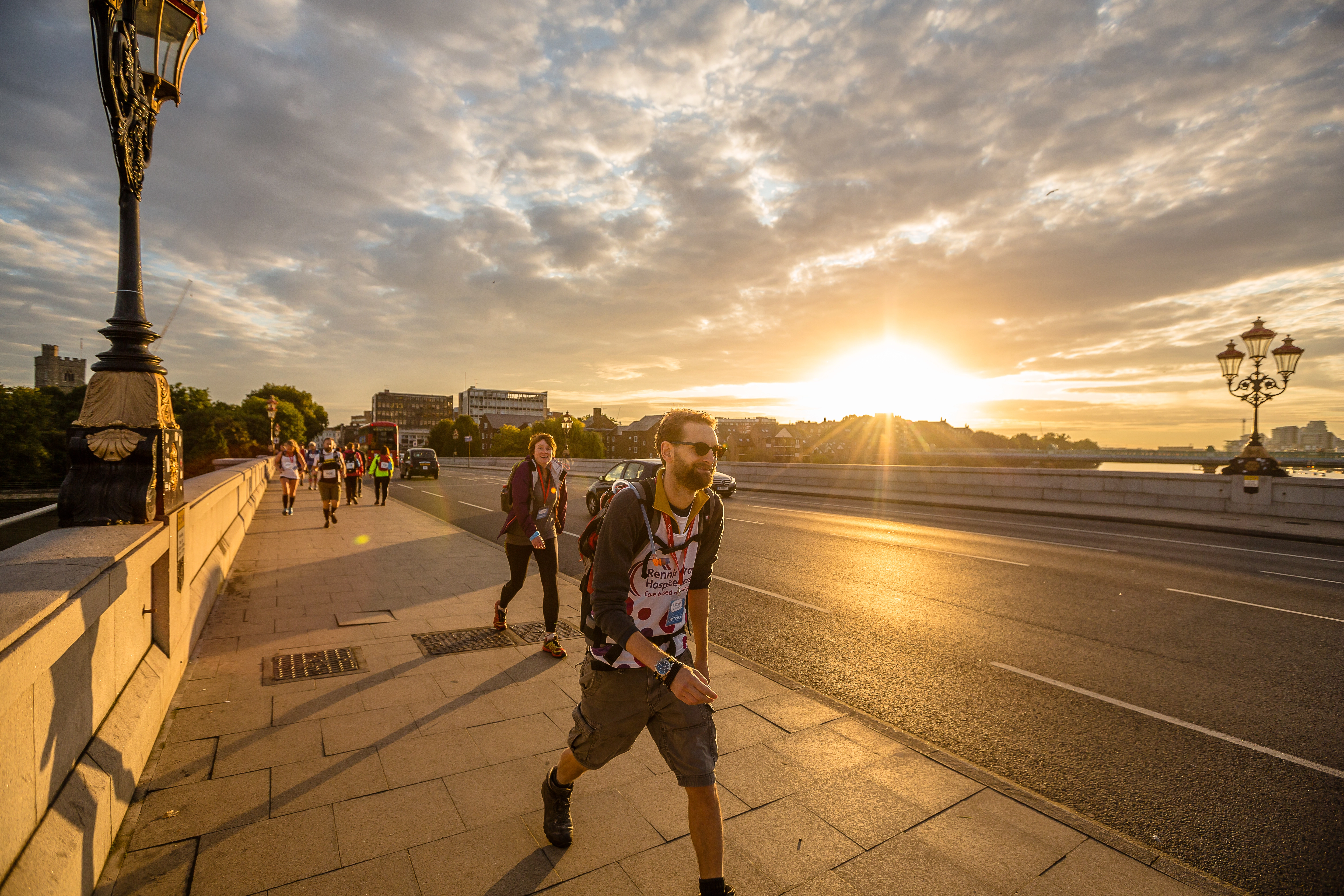Ultra Challenge participants walking across a bridge in London as the sunsets behind them. The walkers are smiling and you can see the city of London's buildings in the background.