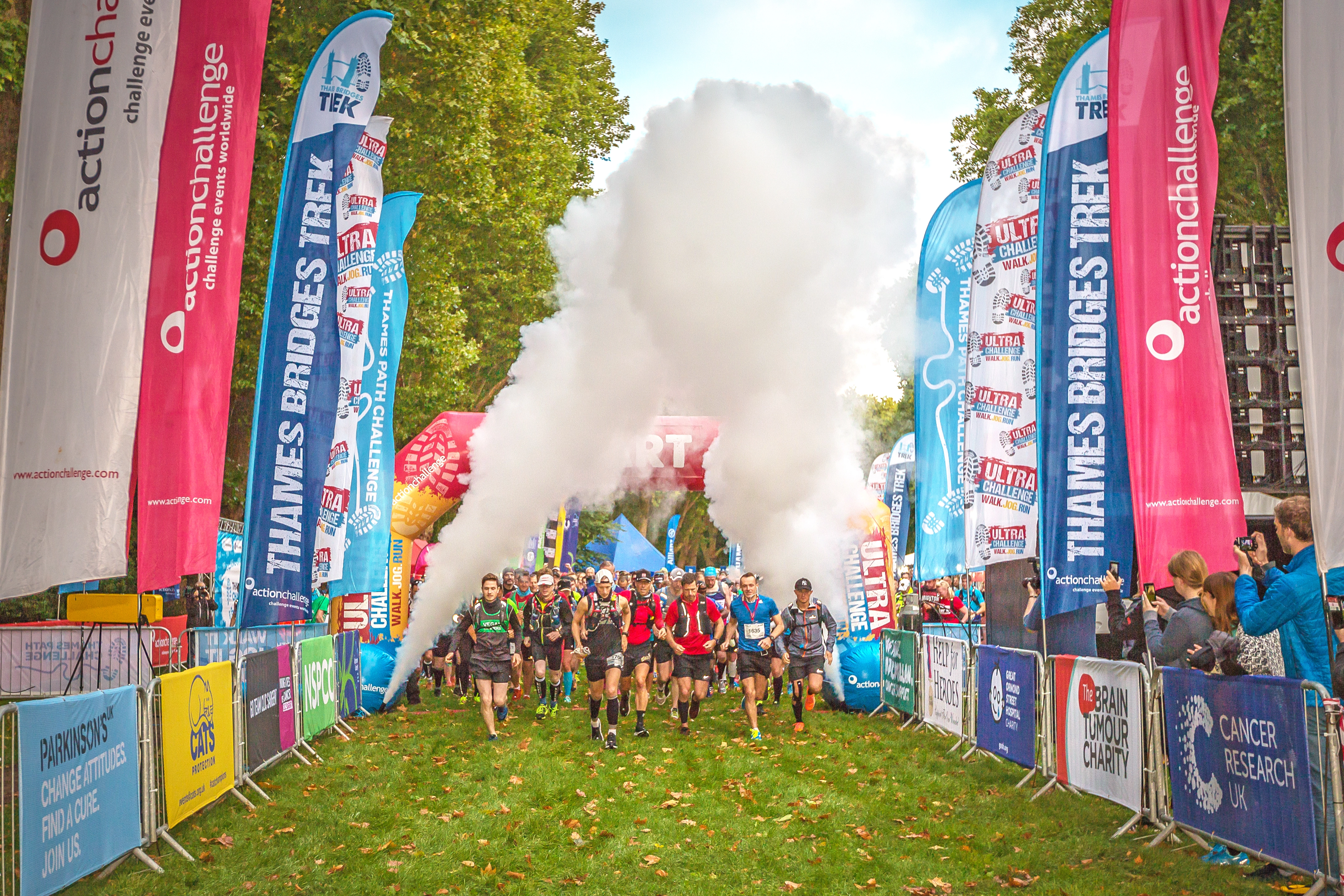 Thames Bridges Trek participants setting off from the start line. People are running and walking while crowds watch from the sides. There are smoke machines and banners.