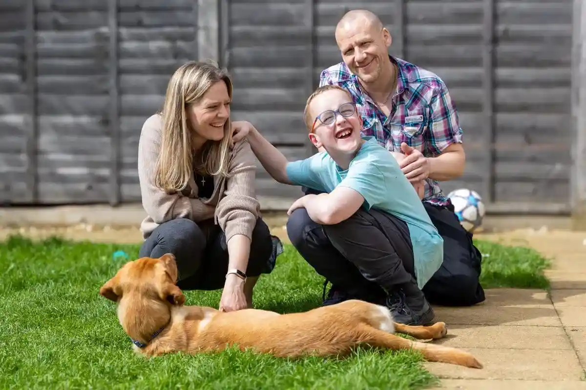 Family Dog Golden Retreiver Laying Down Grass Garden Child Parents Crouched Down Smiling Frontfacing