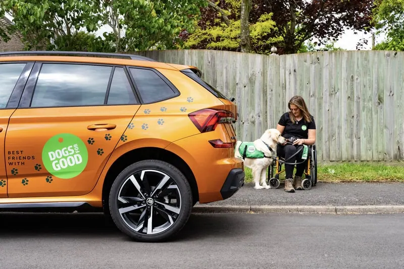Trainer Jess training a Dogs for Good dog outside in the street, next to a Škoda car