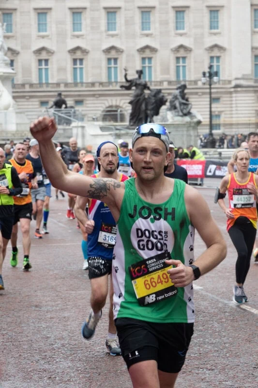 Runner running past statues in London wearing a Dogs for Good vest with fist raised in the air