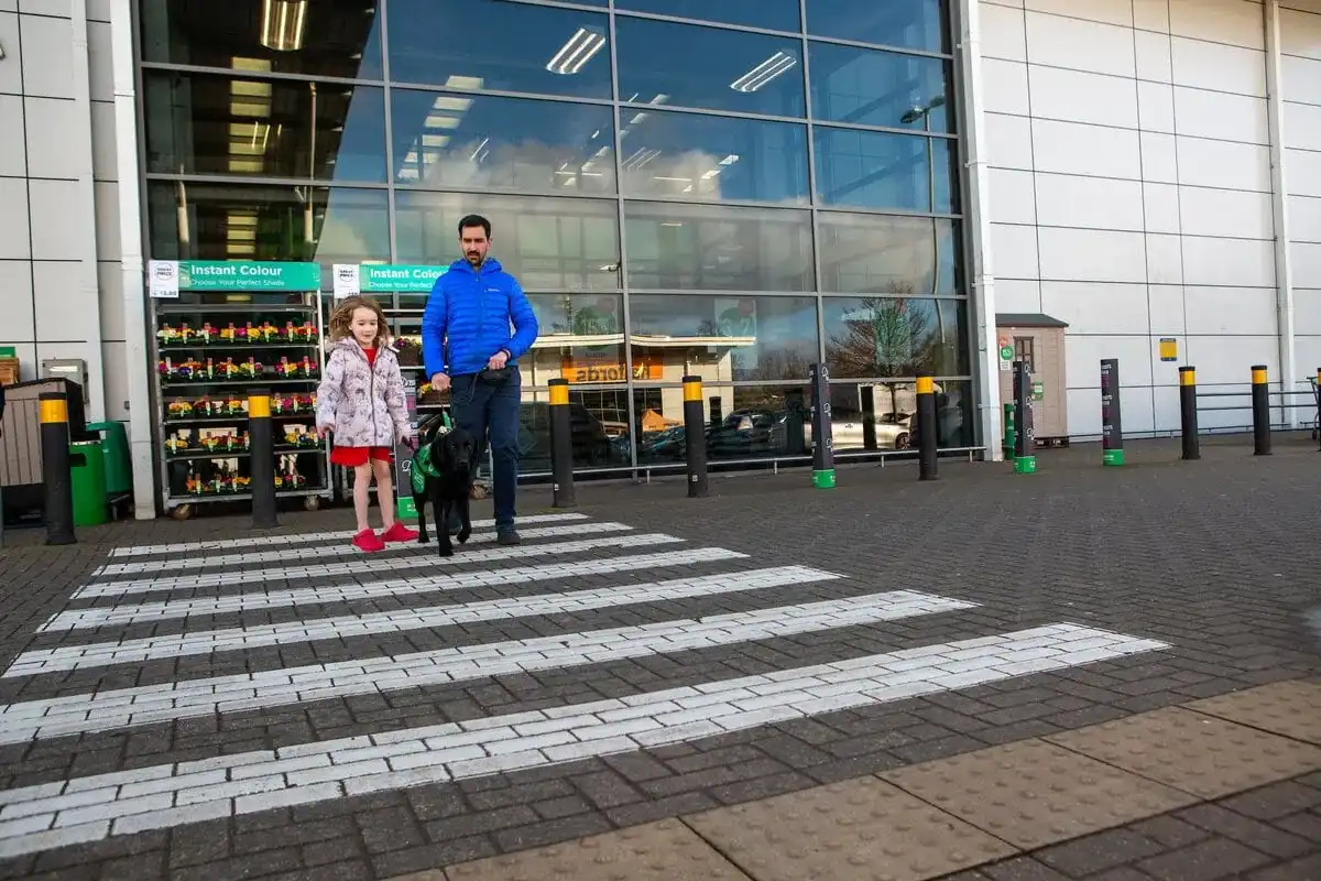 Parent and child walking across zebra crossing in supermarket car park with autism assistance dog on lead