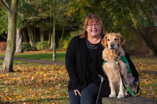 Vicki sitting with her assistance dog Tula a golden retriever in the park 