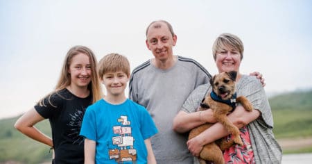 A lady is holding a small dog. She is stood next to a man, a young boy and a young girl.